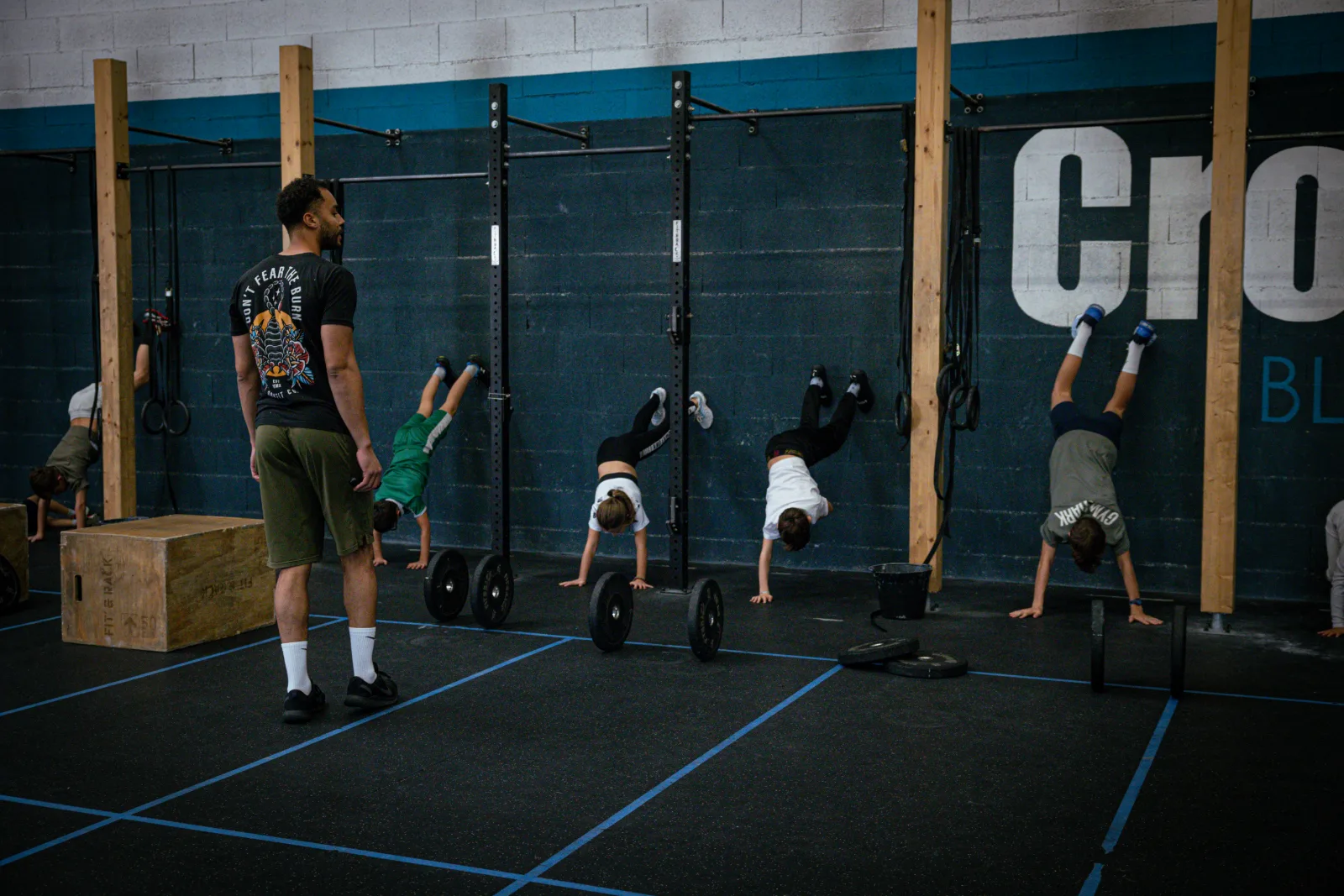 Groupe d'enfants en équilibre contre le mur avec leur coach à la box CrossFit Blue Bird