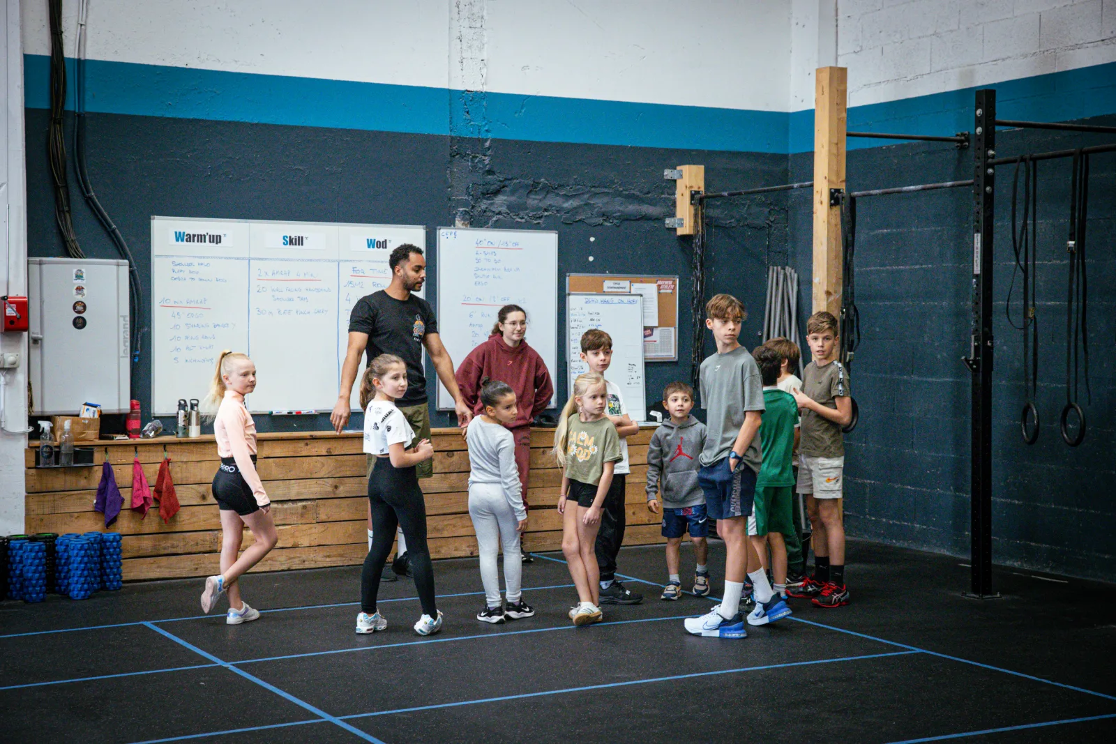 Groupe d'enfants et d'ados réunis devant le tableau du WOD avant la séance
