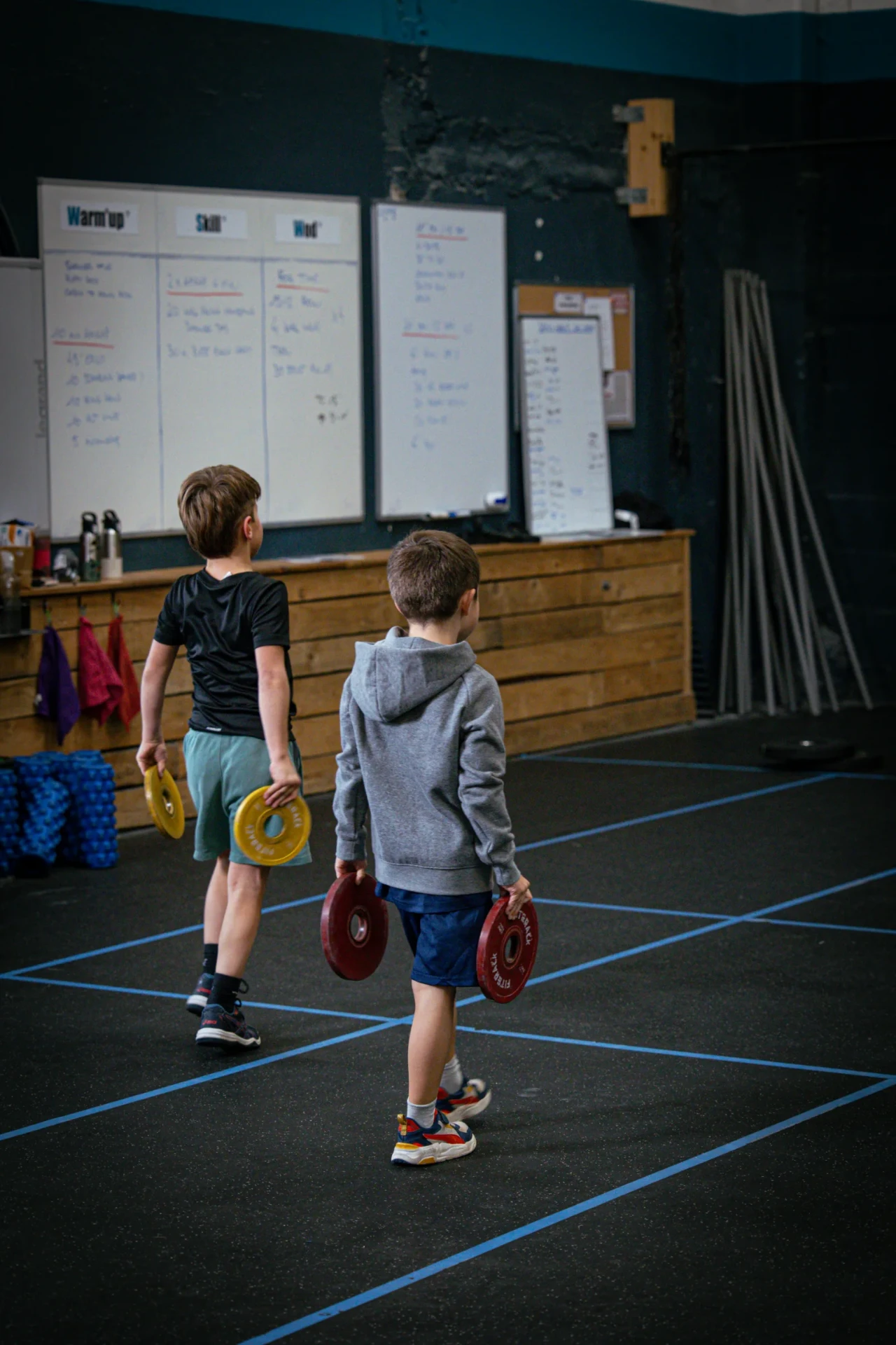 Deux enfants en farmer carry devant le tableau du WOD à la box de Saint-Priest-en-Jarez
