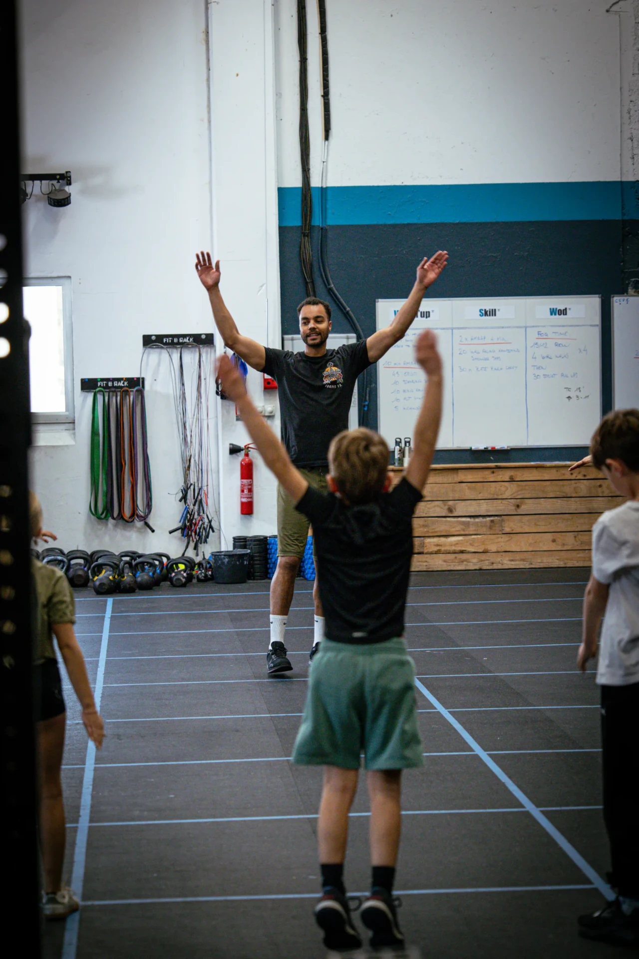 Coach animant l'échauffement bras levés devant les enfants du cours CrossFit Kids