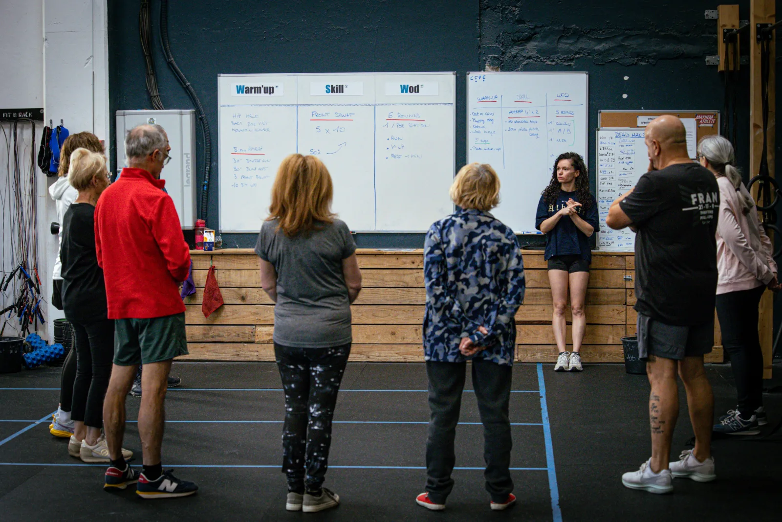 Groupe de seniors écoutant les consignes de la coach devant le tableau du WOD