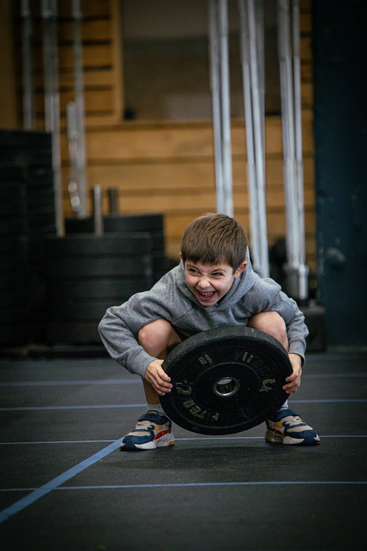 Enfant souriant soulevant un disque pendant le cours de CrossFit pour enfant à Saint-Étienne